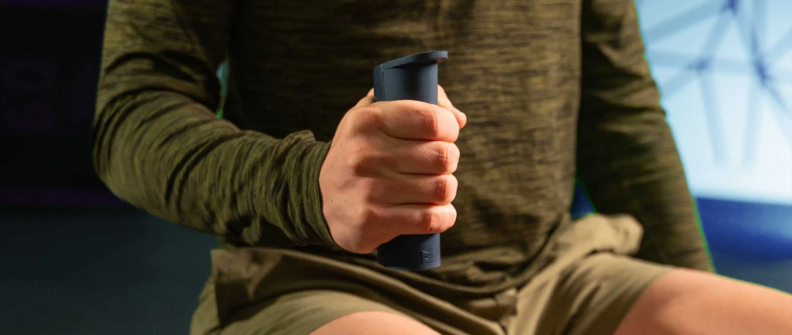A close-up of a young man squeezing a dark blue Kinvent K-Grip connected hand dynamometer to measure his grip strength during a physical assessment