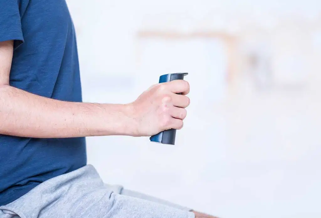 A side view of a man's arm and hand squeezing a blue and grey K-Grip dynamometer to measure grip strength