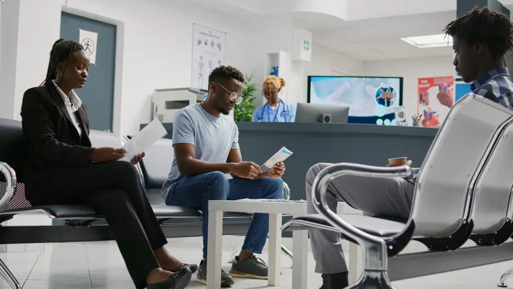 Several young patients sitting and reading documents in a hospital waiting room lobby near the reception desk, preparing for a medical consultation
