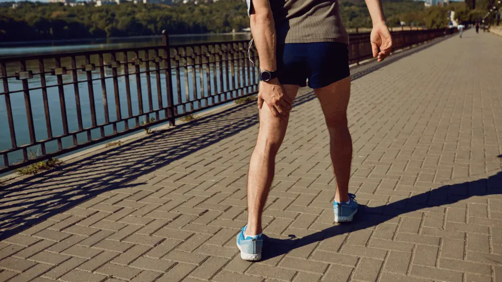 A runner holding the back of his thigh due to a sudden hamstring injury while training outdoors