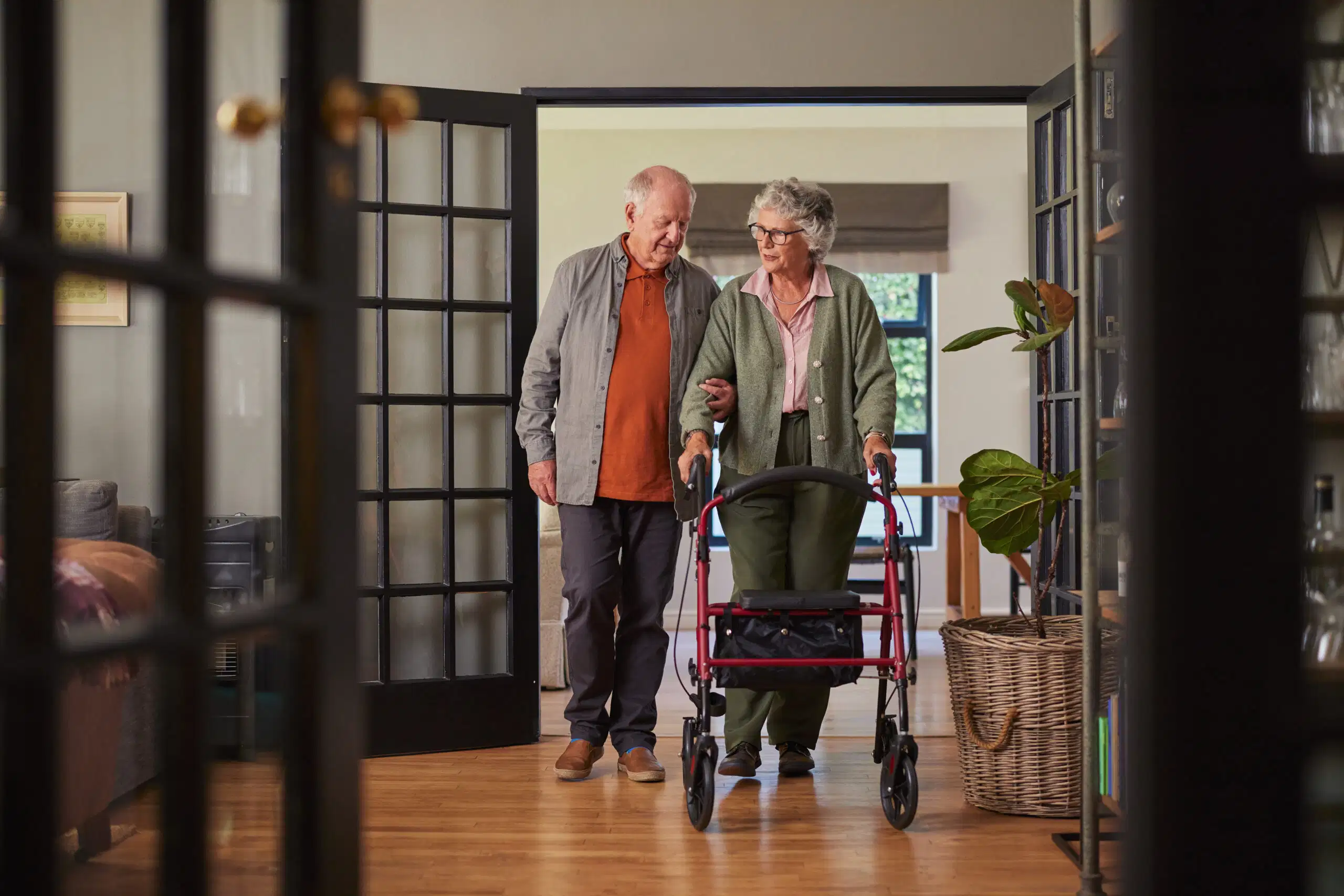 An elderly man helping his wife walk at home using a rollator walker to prevent fall risks