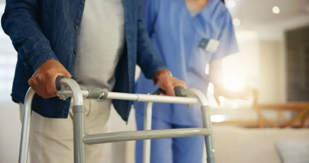 Un homme âgé utilisant un déambulateur pour marcher sous la surveillance attentive d'une infirmière en tenue de soins