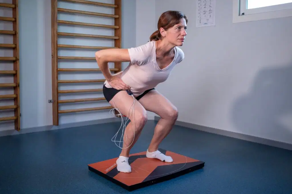 Comprender la EMG de superficie: definición, beneficios y cómo funciona 2 A female athlete performing a squat on Kinvent force plates while equipped with surface EMG sensors on her thigh