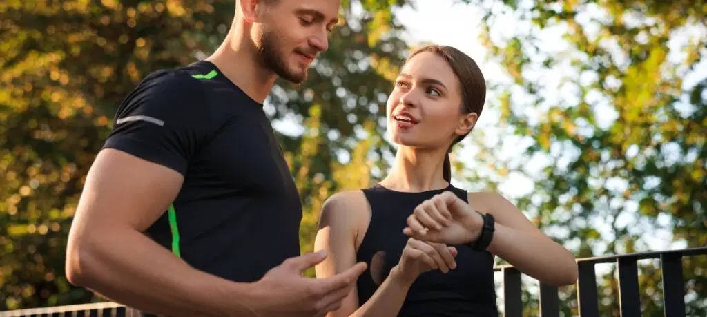 Two athletes outdoors checking performance data on a smartwatch after a training session used as header image for the Kinvent article on shoulder rotator assessment ratios norms and injury prevention for athletes