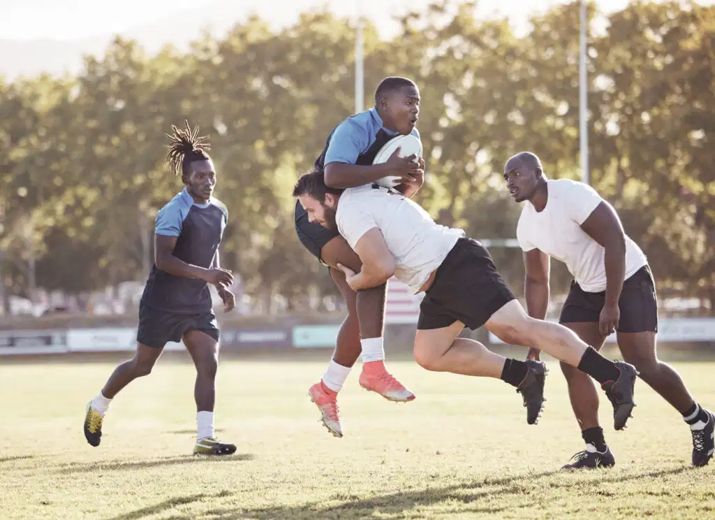 Renforcement des muscles cervicaux pour prévenir les commotions : guide complet 2025 159 Un joueur de rugby en maillot blanc tentant de plaquer un adversaire en plein élan qui porte le ballon, illustrant l'importance du renforcement des muscles cervicaux pour prévenir les risques de commotions cérébrales lors des impacts