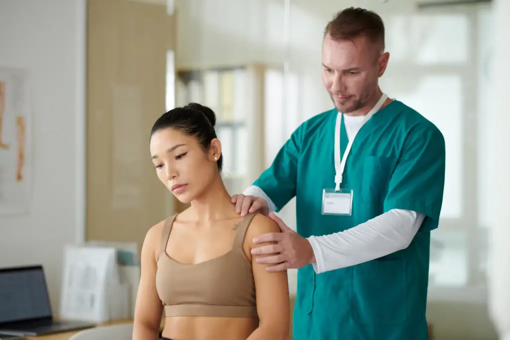 Un kinésithérapeute effectuant une palpation manuelle de l'épaule et du cou d'une patiente assise lors d'une séance d'évaluation de la coiffe des rotateurs