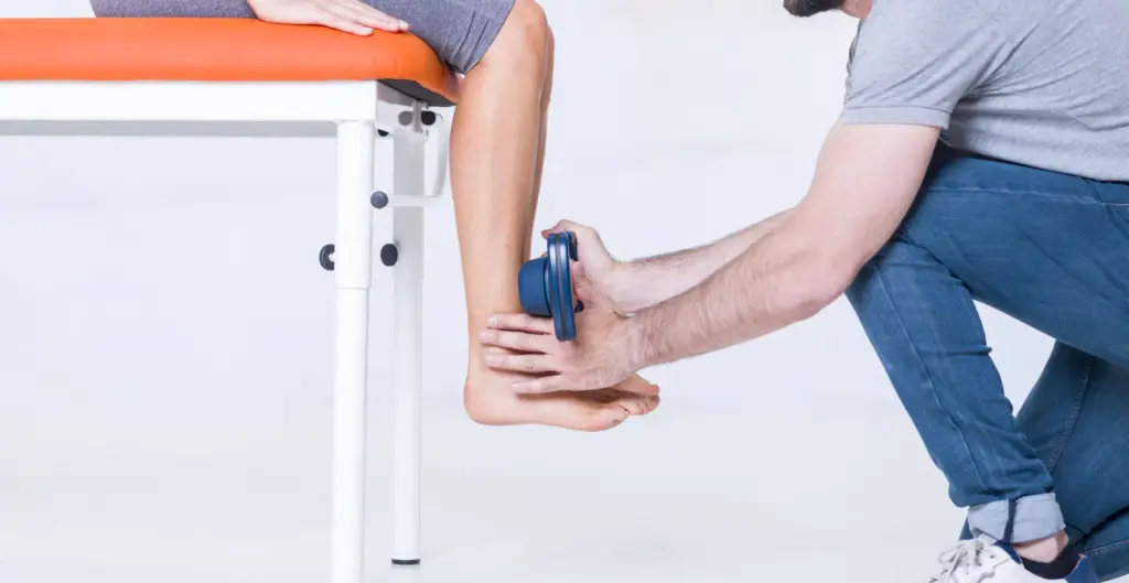 Un professionnel de santé utilise un dynamomètre manuel connecté Kinvent pour évaluer et mesurer la force musculaire au niveau de la cheville d'un patient assis sur une table d'examen