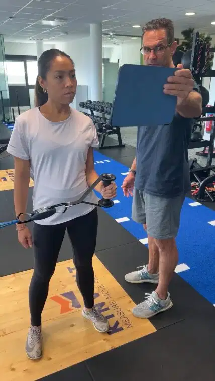 Los cuatro pilares del movimiento humano: movilidad, estabilidad, fuerza y movimiento funcional explicados 6 A coach tracks a woman's shoulder or core strength training on a tablet using a Kinvent connected pull sensor in a gym