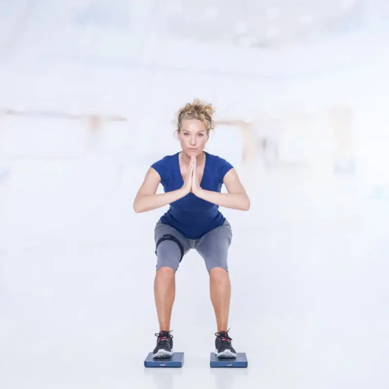 Les 4 piliers du mouvement : mobilité, stabilité, force et mouvement fonctionnel 9 Woman performing a squat on Kinvent force plates with hands together, demonstrating lower body functional movement evaluation