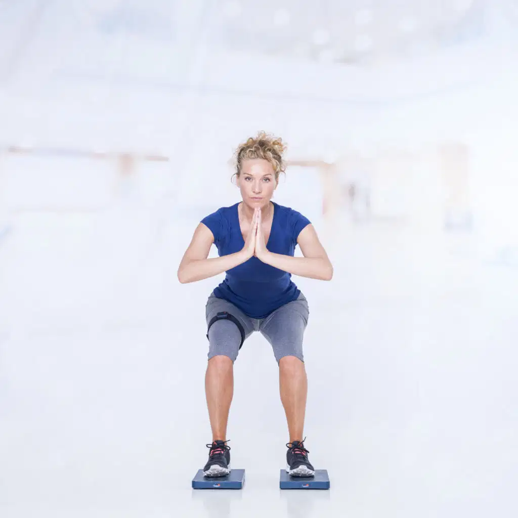 Los cuatro pilares del movimiento humano: movilidad, estabilidad, fuerza y movimiento funcional explicados 8 Woman performing a squat on Kinvent force plates with hands together, demonstrating lower body functional movement evaluation