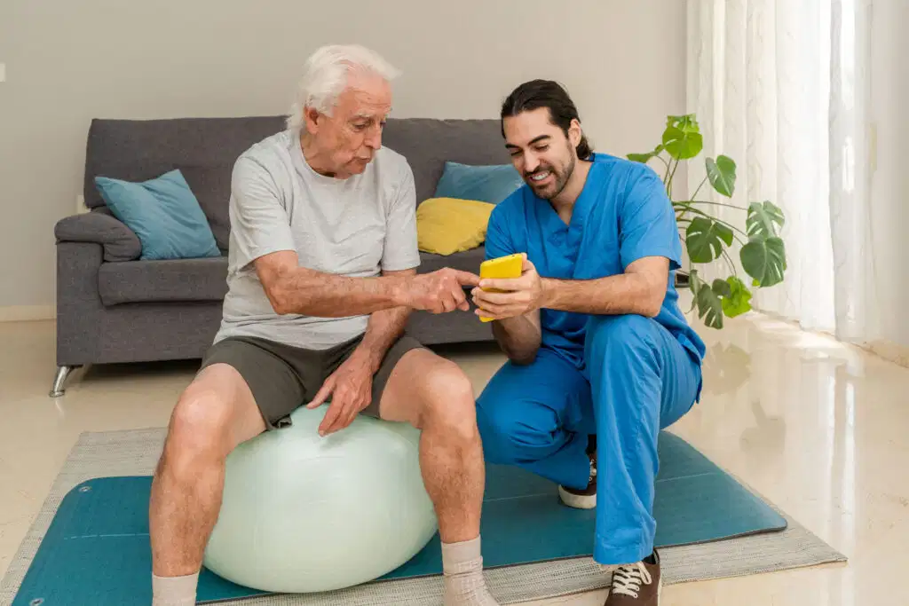 Top 10 tendencias en fisioterapia en 2026 que no te puedes perder 3 A physical therapist guiding a senior patient on a fitness ball using a smartphone app, illustrating hybrid care trends in 2026