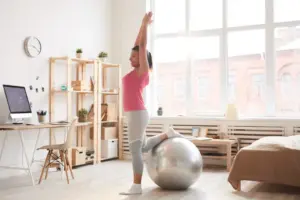 Los cuatro pilares del movimiento humano: movilidad, estabilidad, fuerza y movimiento funcional explicados 1 Woman balancing on one leg with her other leg on a fitness ball and arms raised, demonstrating a stability exercise at home