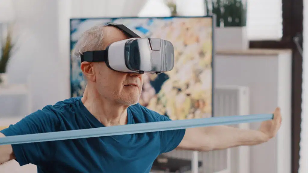 Top 10 tendencias en fisioterapia en 2026 que no te puedes perder 5 A senior patient wearing a virtual reality headset while performing a resistance band workout, illustrating VR physical therapy trends in 2026