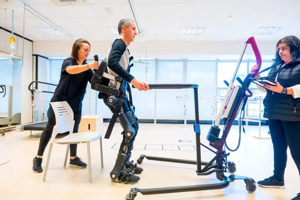Top 10 tendencias en fisioterapia en 2026 que no te puedes perder 6 A patient training with a mechanical exoskeleton assisted by physical therapists, showcasing robotic rehabilitation trends in 2026