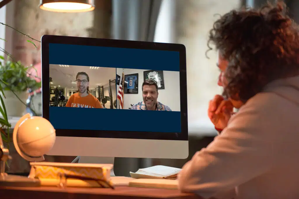 Top 10 tendencias en fisioterapia en 2026 que no te puedes perder 8 A person from behind watching an online physical therapy webinar on a desktop computer screen, displaying two speakers talking during a video conference, illustrating upcoming trends in physiotherapy digital learning