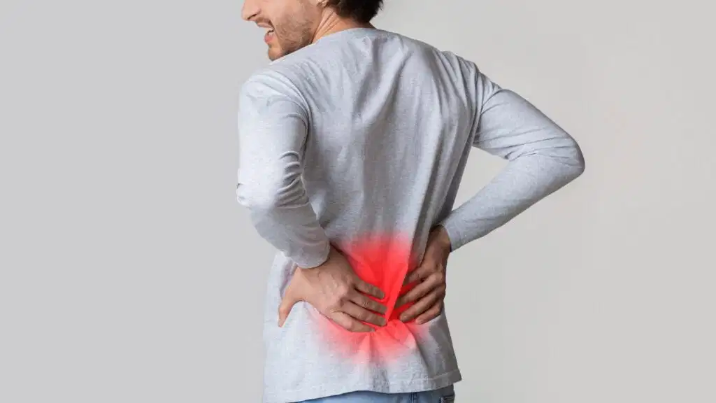 Man holding his lower back with a red glowing area representing low back pain or lumbar inflammation