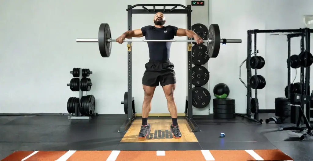 Weightlifter measuring barbell speed with a VBT connected sensor during a training session in a gym