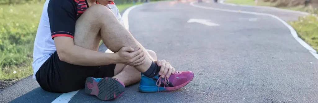 Ankle Sprain Treatment: Protocols & Objective Assessment Tools 22 Injured runner holding his lower leg on the ground, illustrating the need for ankle sprain rehabilitation