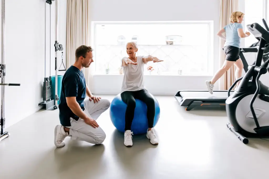 How to Design a High-Performance Rehab Gym: The Complete Guide for Physical Therapists 13 Physical therapist guiding a senior patient during balance and core stability exercises on a Swiss ball in a rehabilitation clinic