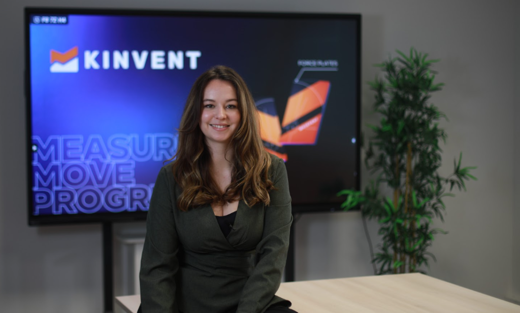 Léa, a smiling Kinvent Customer Success representative, seated in front of a Kinvent branding screen in an office