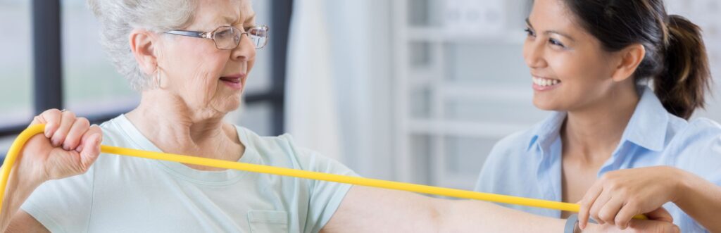 A smiling physical therapist guiding an elderly female patient during a resistance band exercise to improve patient retention