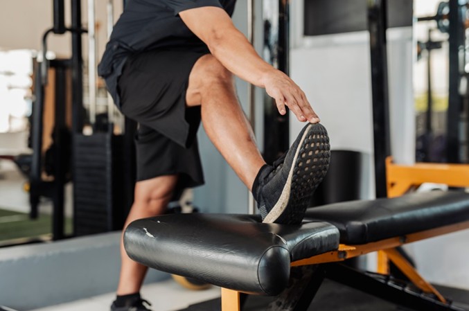 Man stretching his hamstring on a padded bench in a physical therapy clinic