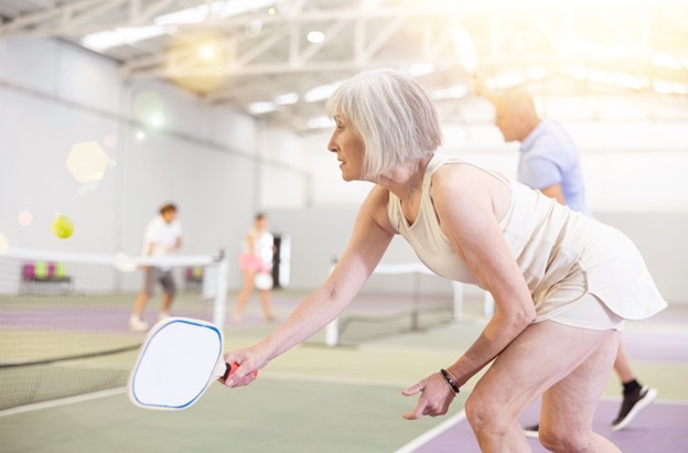 Senior woman playing pickleball or paddle tennis on an indoor court, ready position
