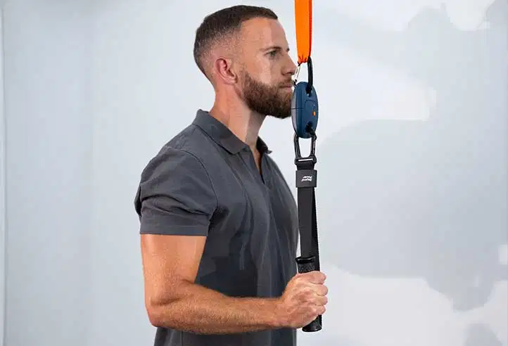 Vista lateral de un hombre realizando un ejercicio de tracción o una evaluación de tiro mediante un sensor de fuerza K-Pull sujeto a una correa suspendida naranja y una empuñadura vertical
