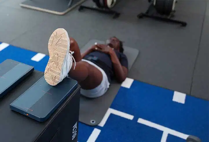 Pathology-Specific Assessments 34 High-angle view of an athlete lying on a training mat, performing a single-leg bridge exercise with one foot resting on a Kinvent force plate placed on an elevated box
