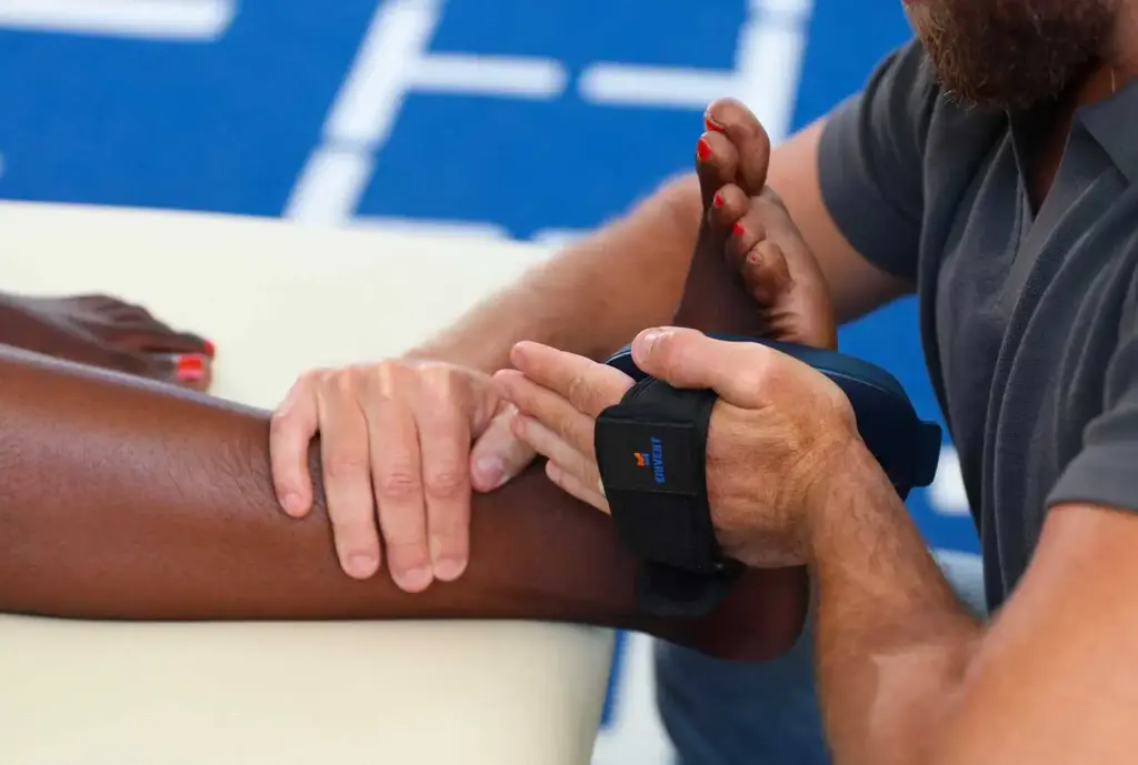 Rehabilitación específica por zona del cuerpo 44 Primer plano de un profesional sanitario realizando una prueba de fuerza de tobillo y pie a un paciente mediante un sensor de fuerza manual Kinvent con correa para evaluar la fuerza durante una sesión de rehabilitación localizada.