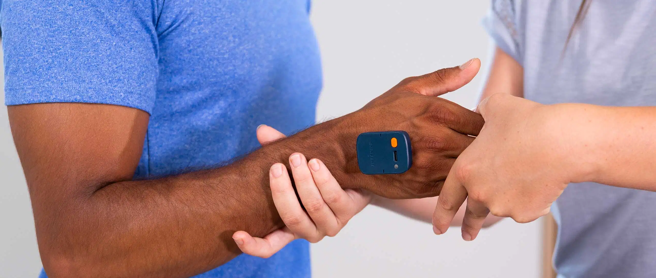 A close-up of a practitioner's hands guiding a patient's wrist and hand movement during a physiotherapy session, with a blue K-Move sensor attached to the back of the patient's hand
