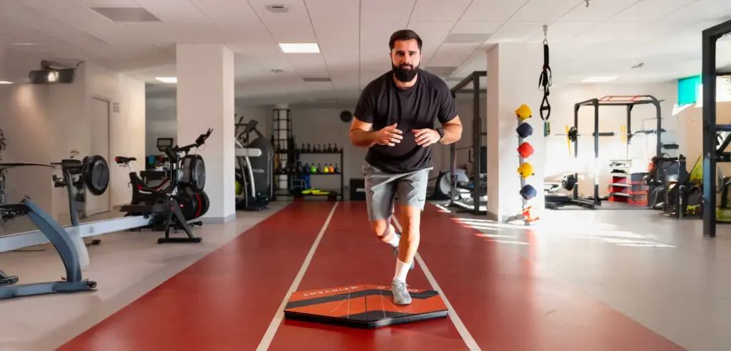 An athlete performing a single-leg stability and movement assessment on an extra-large Kinvent K-Deltas XL force plate inside a gym