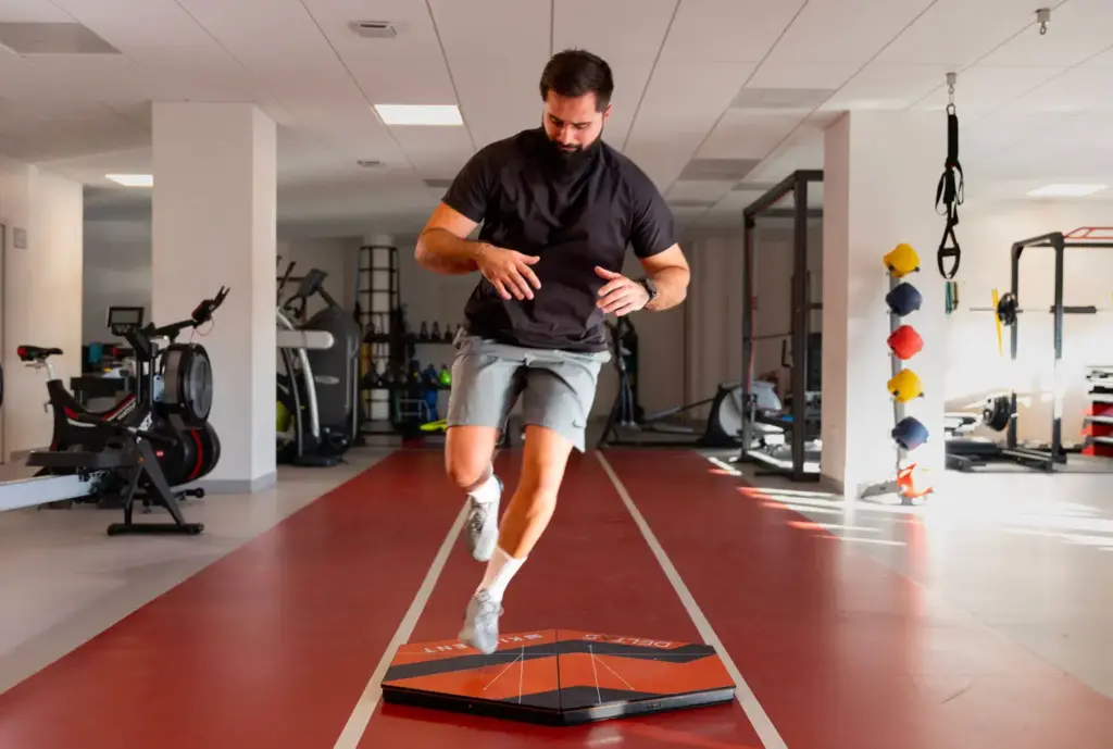 A male patient performing a single-leg stability test on extra-large Kinvent force plates inside a gym for comprehensive biomechanical assessment