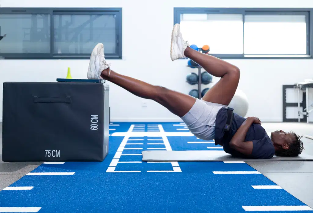 便携式测力板K-Force Plates 43 An athlete lying on a mat, performing a single-leg glute bridge with one foot resting on a Kinvent force plate placed on top of a black plyometric box