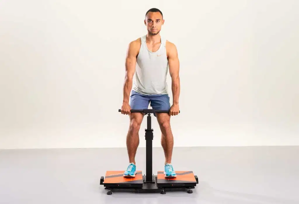 A front-view studio shot of a male athlete performing an Isometric Mid-Thigh Pull (IMTP) strength assessment while standing on orange and black Kinvent force plates against a solid white background