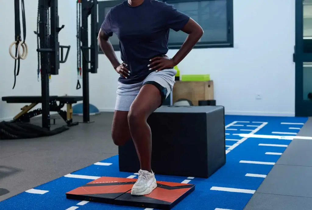 An athlete performing a single-leg Bulgarian split squat for ACL rehabilitation with one foot on a large Kinvent connected force plate and a wireless sensor strapped to the thigh