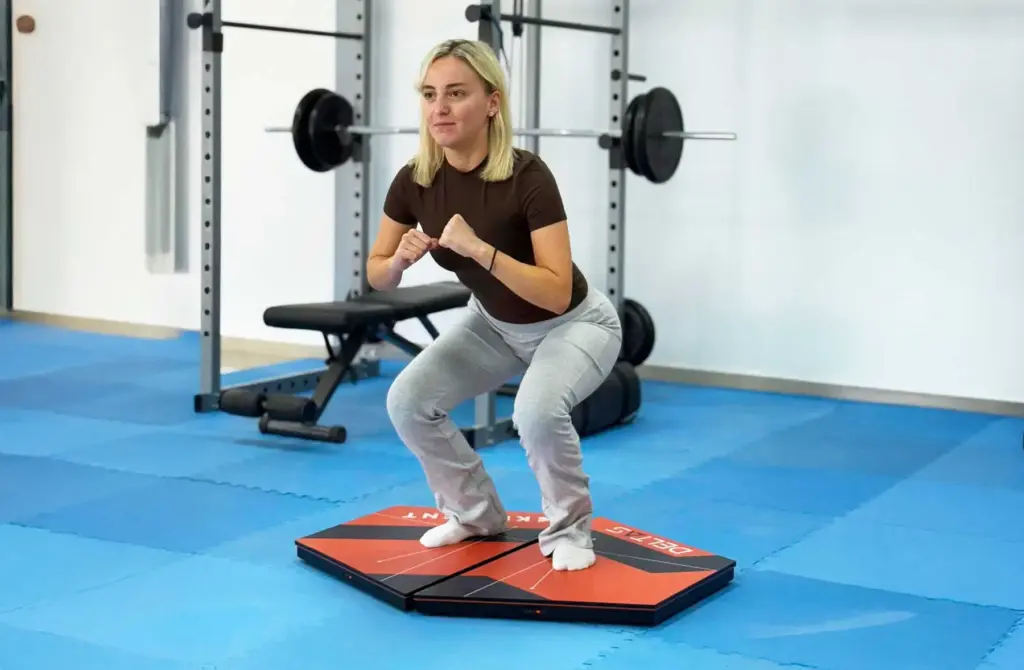 A female athlete performing a squat exercise on Kinvent K-Deltas XL extra-large connected force plates inside a training facility, analyzing force distribution and lower-body stability